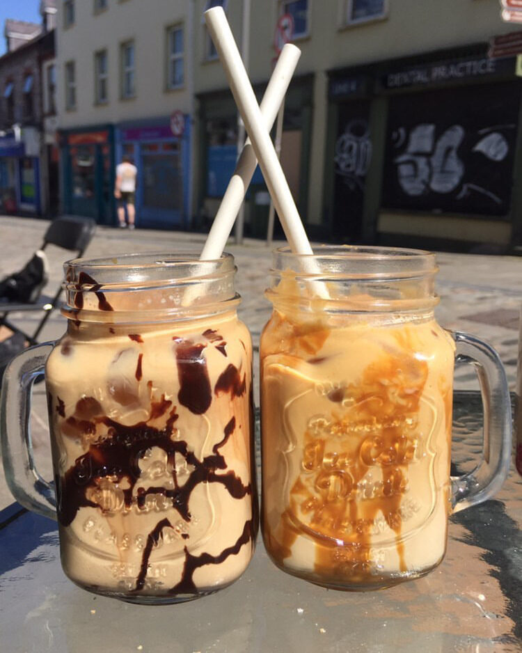 Two iced coffees in mason jars, one with chocolate sauce and one with caramel, on an outdoor table