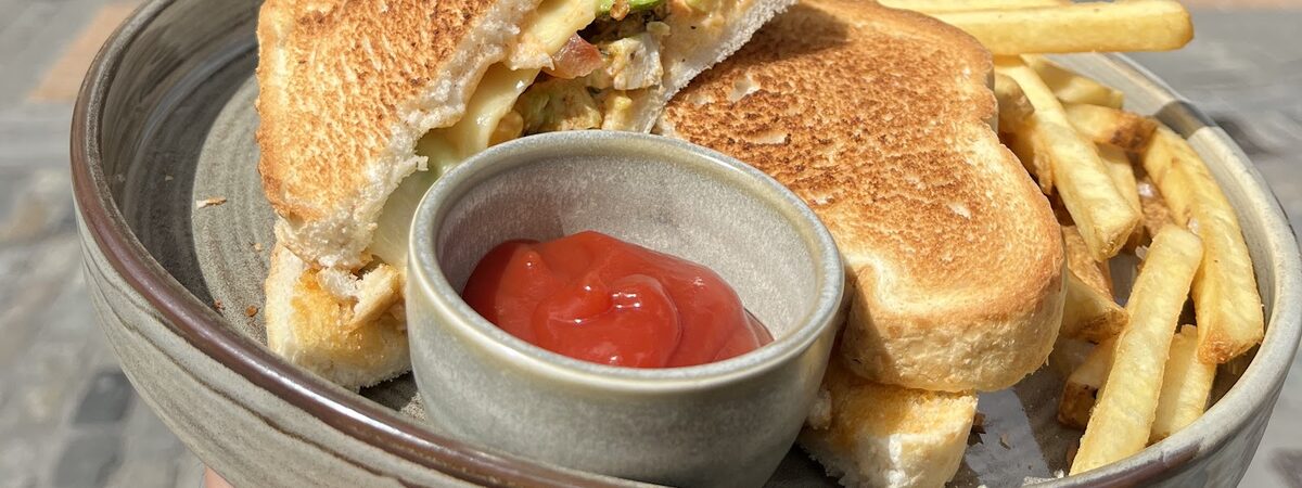 A toasted sandwich and chips on a grey ceramic plate with a pot of ketchup