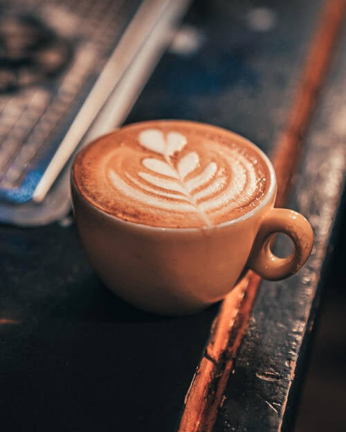 A cup of coffee with a leaf pattern in the milk, on a dark counter